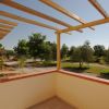 Balcone con pergolato in legno, vista su un giardino con alberi e cielo sereno.