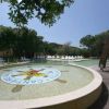 Una fontana circolare con un disegno al centro e lettini intorno, immersa nel verde.