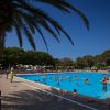 Piscina con persone che nuotano, ombrelloni colorati e palme sullo sfondo.
