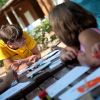 Bambini e un adulto seduti attorno a un tavolo all'aperto mentre disegnano.